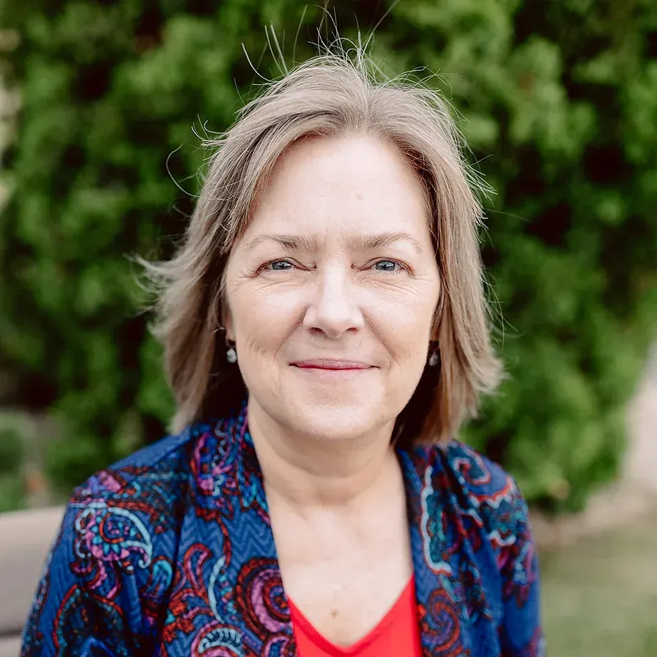 A woman in a blue jacket and red shirt is smiling for the camera.