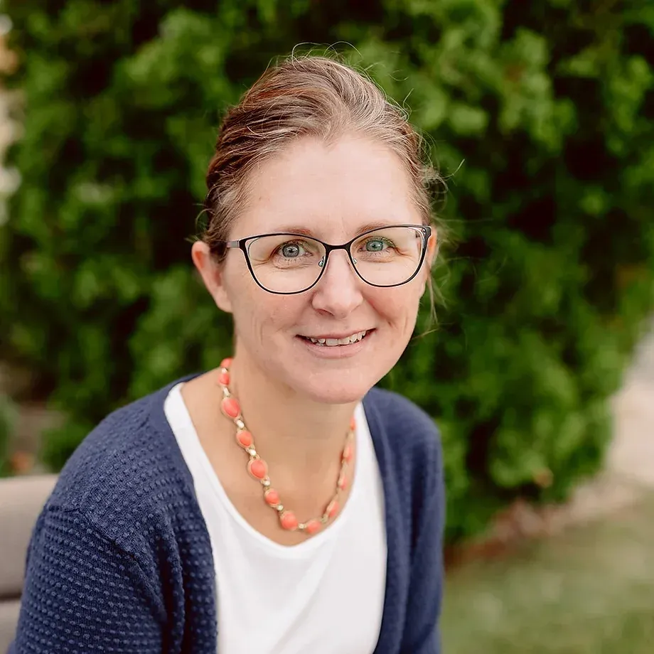 A woman wearing glasses and a necklace is smiling for the camera.