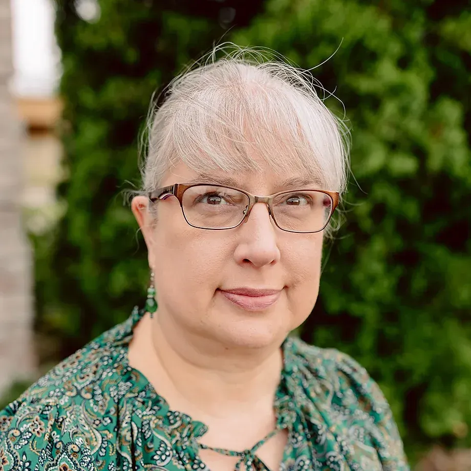 A woman wearing glasses and a green shirt is smiling for the camera.