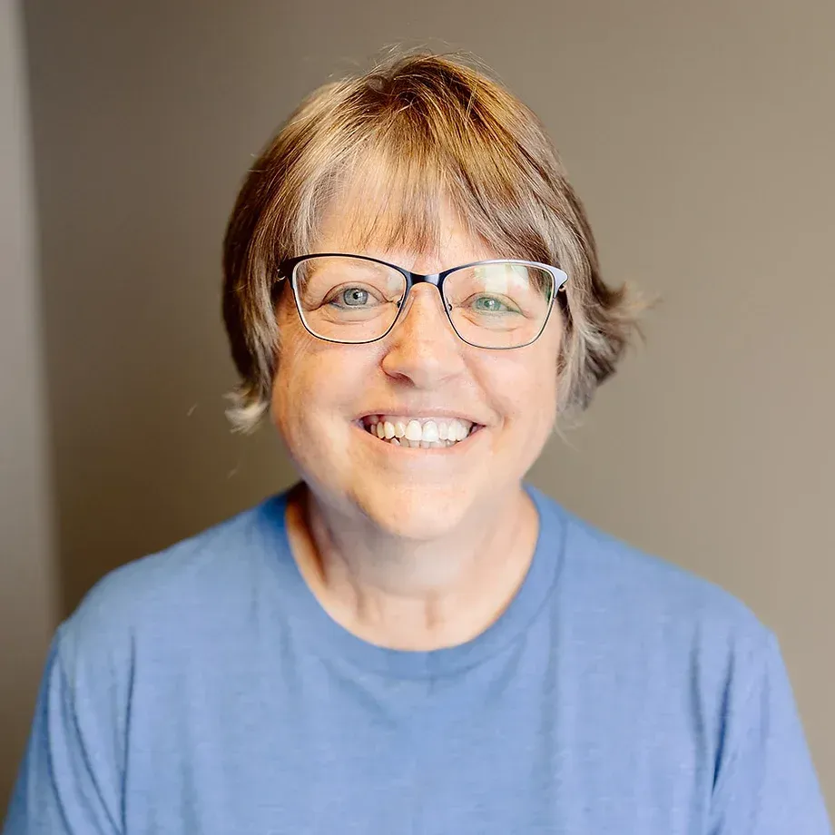 A woman wearing glasses and a blue shirt is smiling for the camera.