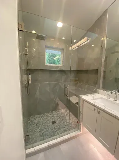 A modern bathroom with a glass-enclosed shower featuring stone pebble flooring, grey tile walls, and a white vanity.