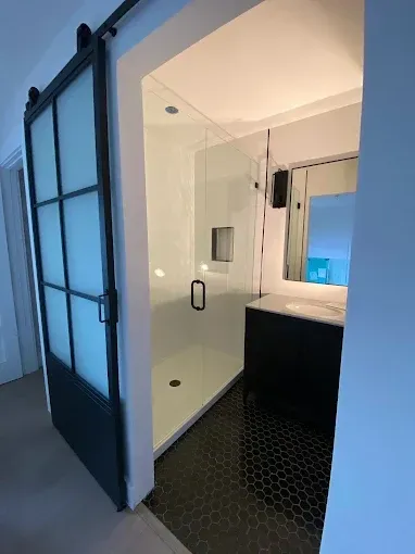 A bathroom featuring a black-framed sliding barn door, a walk-in glass shower, and a vanity with a mirror.