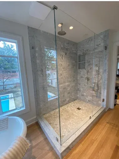 A modern walk-in shower with a glass enclosure, light-colored tile walls, a pebble-stone floor, and a rain-style showerhead.