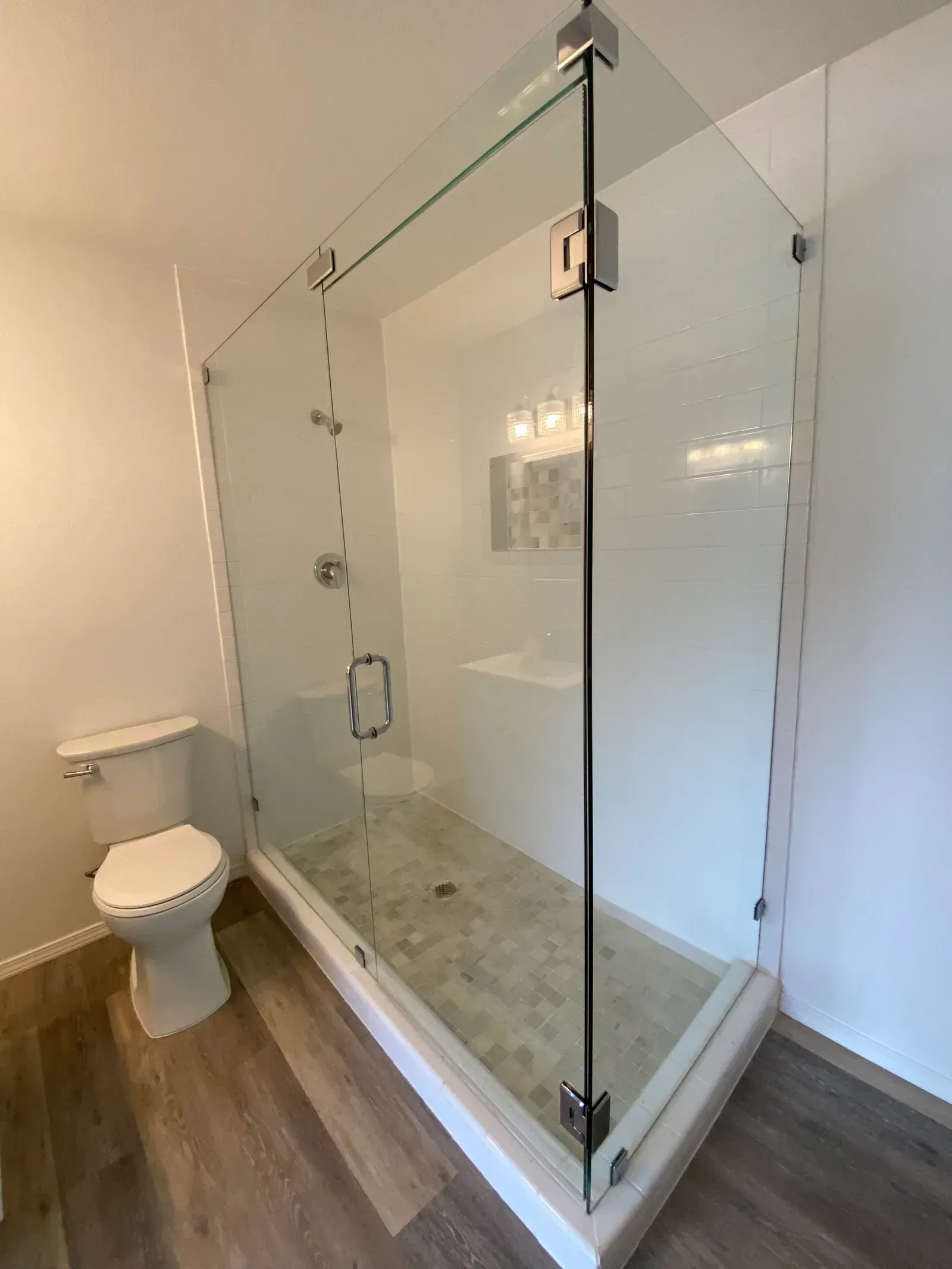 A modern bathroom with a glass-enclosed walk-in shower featuring a pebble tile floor, next to a white toilet.