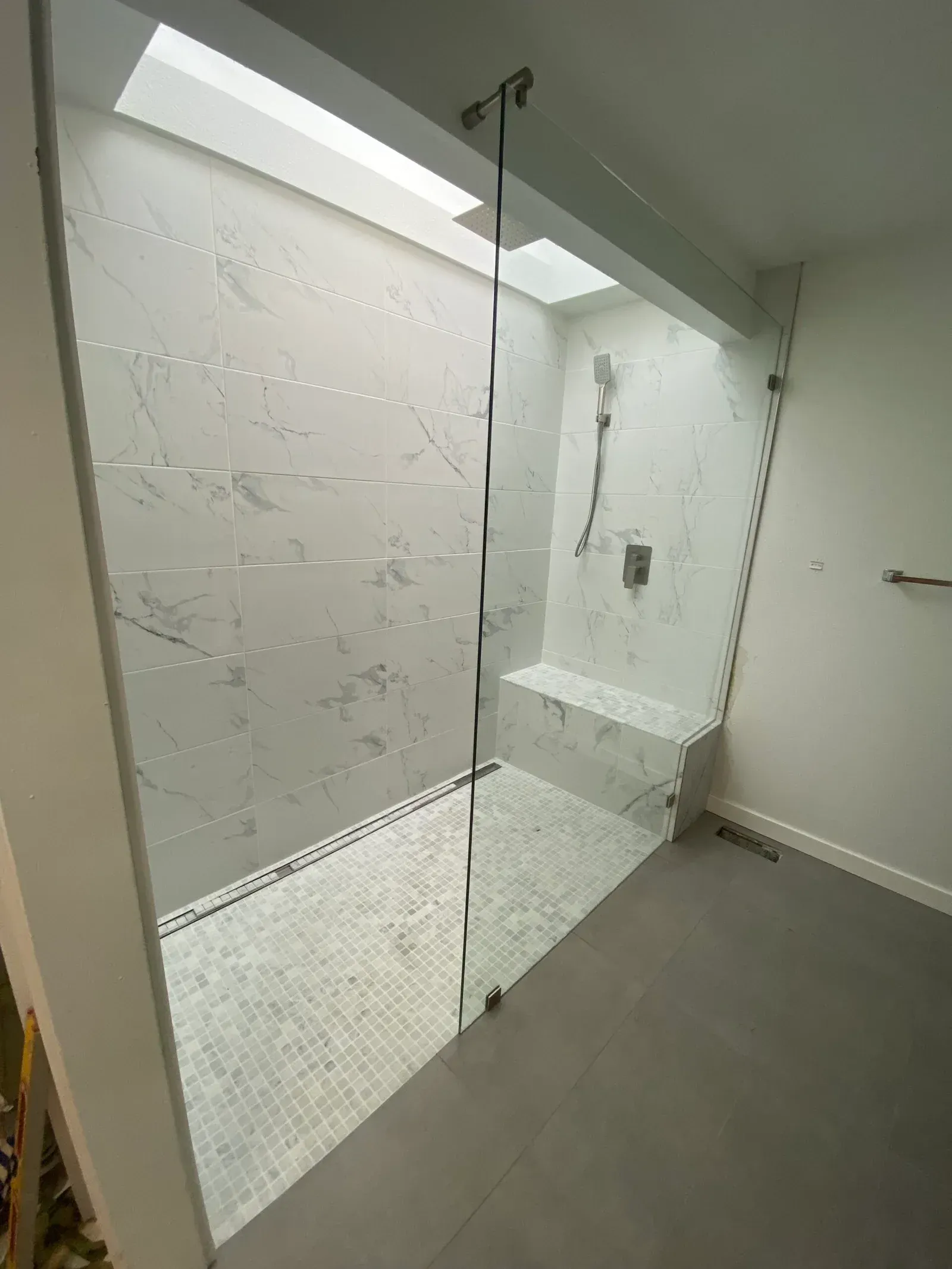 A walk-in shower with marble-look wall tiles, a mosaic tile floor, a glass partition, and a built-in bench.