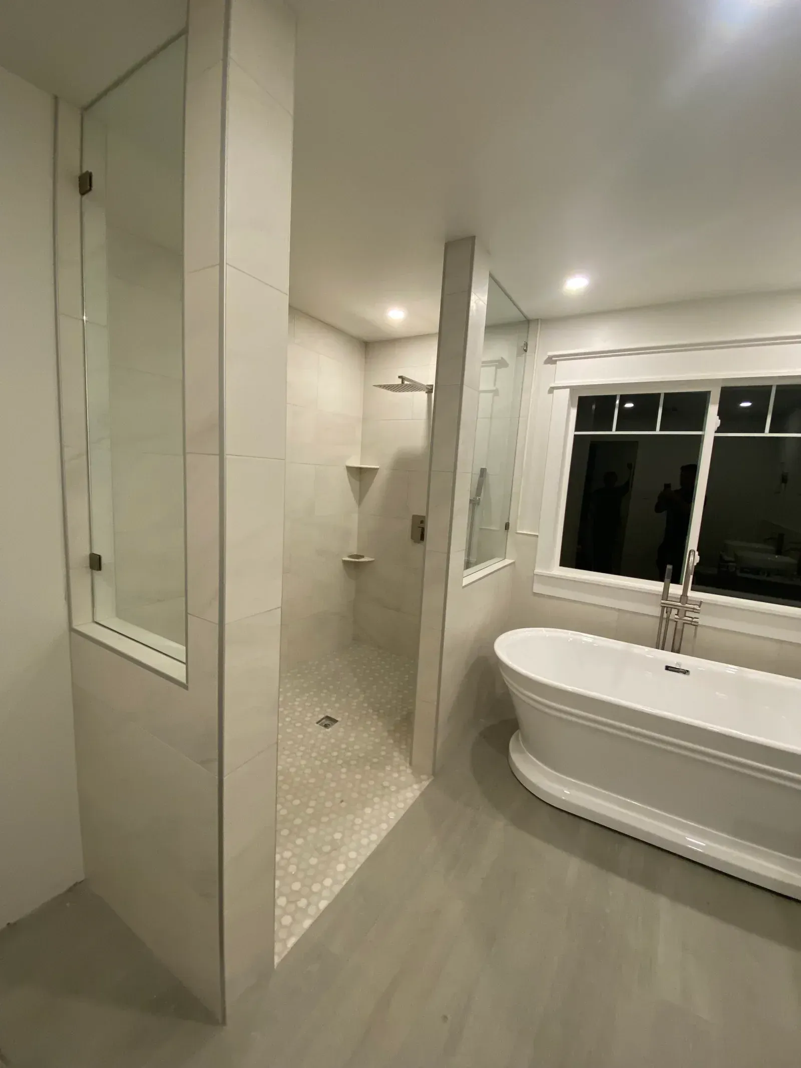 A modern bathroom with a white freestanding tub next to a tiled walk-in shower enclosed by glass panels.