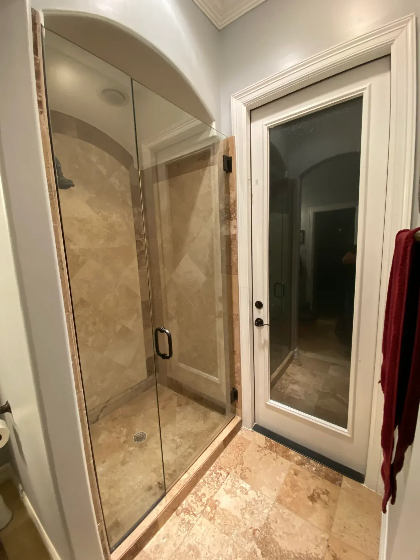 A shower with glass walls and a glass-paneled door in a bathroom with beige tile floors and white trim.