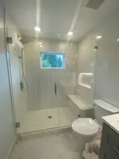 Modern white-tiled bathroom featuring a glass walk-in shower with a built-in bench and a toilet.