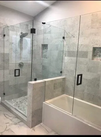 A modern bathroom featuring a glass-enclosed shower stall next to a bathtub, both tiled in light gray stone.