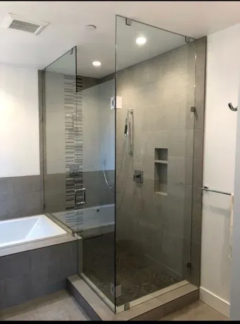 A walk-in shower with a glass enclosure, tiled walls, a built-in niche, and a handheld sprayer next to a white bathtub.