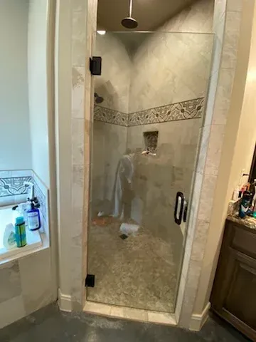 A frameless glass shower door with black hardware, set in a tiled bathroom with neutral walls.