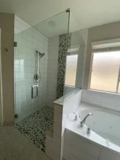 Modern bathroom with a glass-enclosed walk-in shower featuring pebble flooring, next to a white built-in soaking tub.