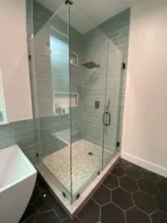 A modern glass shower enclosure with gray subway tiles, a pebble floor, and black hardware in a bathroom with hex tiles.