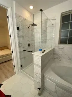 A bathroom with a white marble-tiled walk-in shower featuring a glass door and a soaking tub next to it.