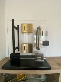 A display of various hardware, including door handles, hinges, and mounting brackets, mounted on a clear acrylic stand.