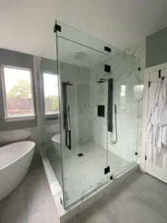 A modern bathroom with a glass-enclosed shower, marble tile, a freestanding bathtub, and gray walls.