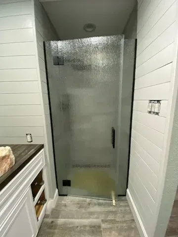 A walk-in shower with a frosted glass door, white shiplap walls, and wood-look tile flooring in a modern bathroom.