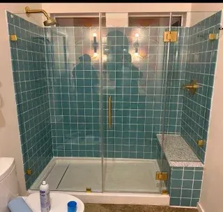 A glass shower enclosure with blue square wall tiles, brass hardware, and a stone-topped bench.