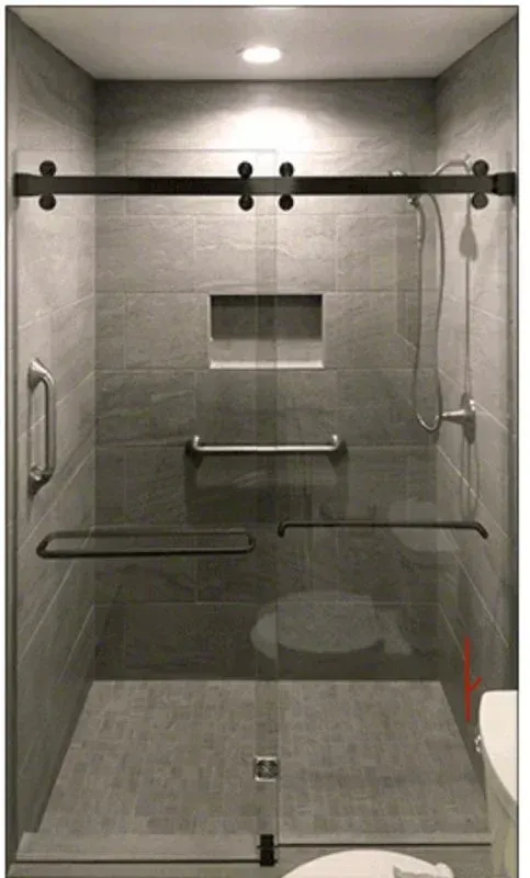 A modern walk-in shower with grey tiled walls, a sliding glass door, a wall-mounted grab bar, and a recessed soap niche.