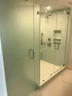 A walk-in shower with a frosted glass door next to a clear glass panel, featuring a built-in shelf and chrome fixtures.