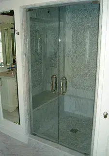 A modern, white-tiled walk-in shower with clear glass double doors and an interior stone bench, next to a vanity mirror.