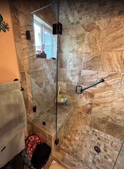 A walk-in shower with stone tile, a built-in bench, glass partition, and a black grab bar on the back wall.