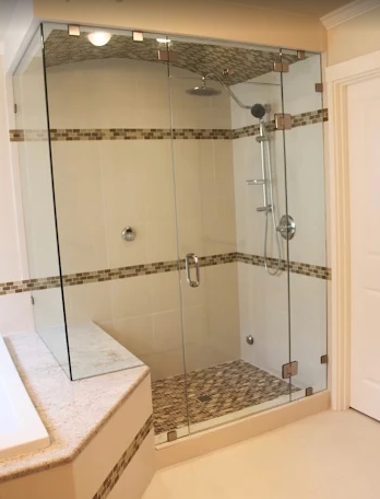 A modern glass-enclosed shower with pebble tile flooring and decorative mosaic accents in a beige bathroom.