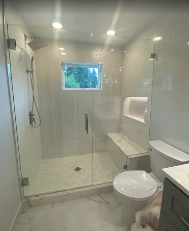 Modern bathroom with a glass-enclosed walk-in shower, a white toilet, and marble-look tile flooring.