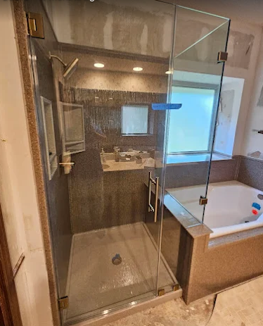 A walk-in shower with a glass door next to a white bathtub in a tiled bathroom with a window.