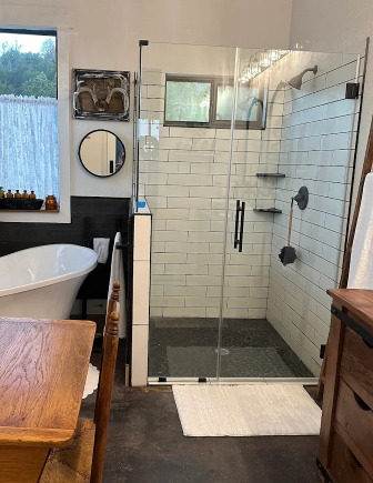 A modern bathroom featuring a white freestanding tub, a glass-enclosed shower with white tiles, and a wooden table.