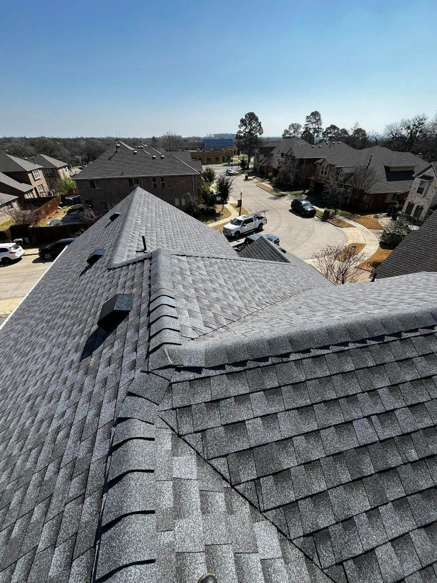 Gray shingle roof, angled view. Houses and vehicles are in the distance on a sunny day.