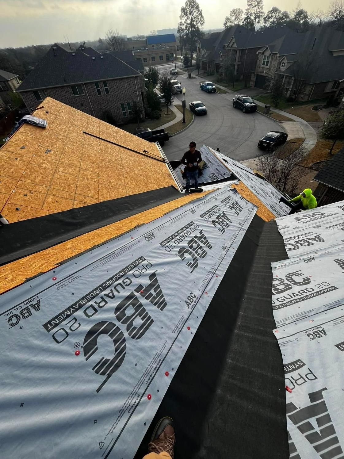 Roofers installing shingles on a residential roof in a neighborhood.
