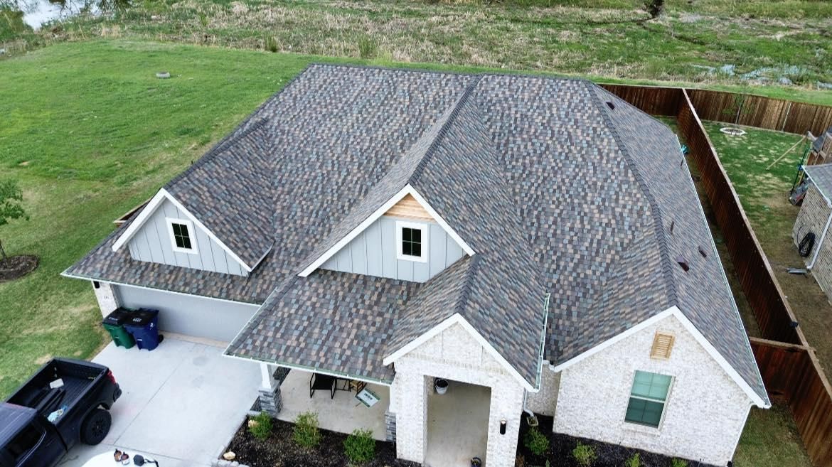 Aerial view of a gray-roofed house with white brick, blue siding, and a wooden fence.