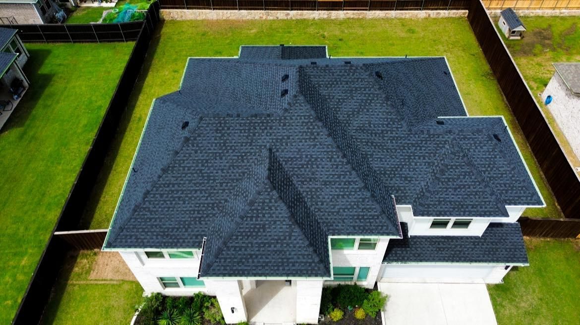 Aerial view of a white house with a dark blue shingle roof, surrounded by green lawn and a black fence.