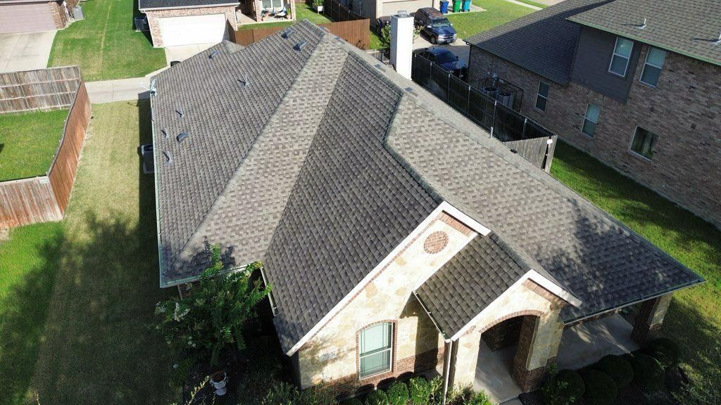 Overhead view of a house with a gray shingle roof, green lawn, and beige brick exterior.