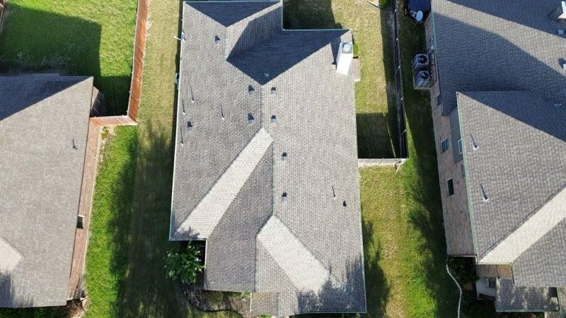 Aerial view of a gray-roofed house with lush green lawn, next to other similar houses.