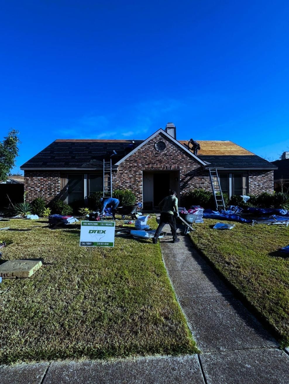 House roof being replaced. Roofers work on a brick home under a clear blue sky.