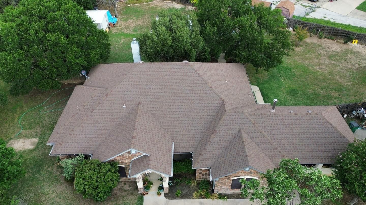 Aerial view of a brown-roofed house with landscaping and trees.