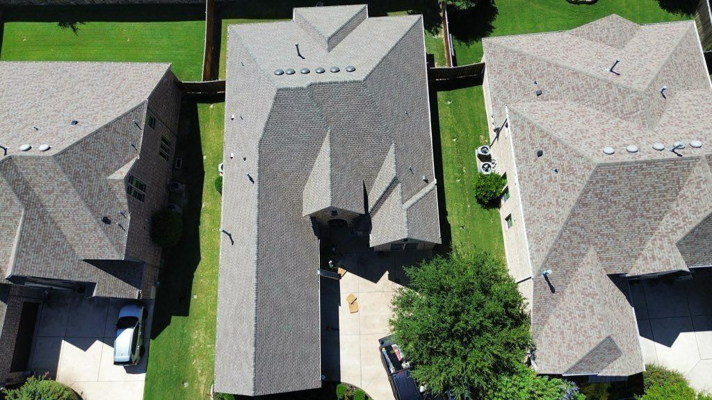 Aerial view of three houses with gray roofs and green lawns, closely spaced in a residential area.