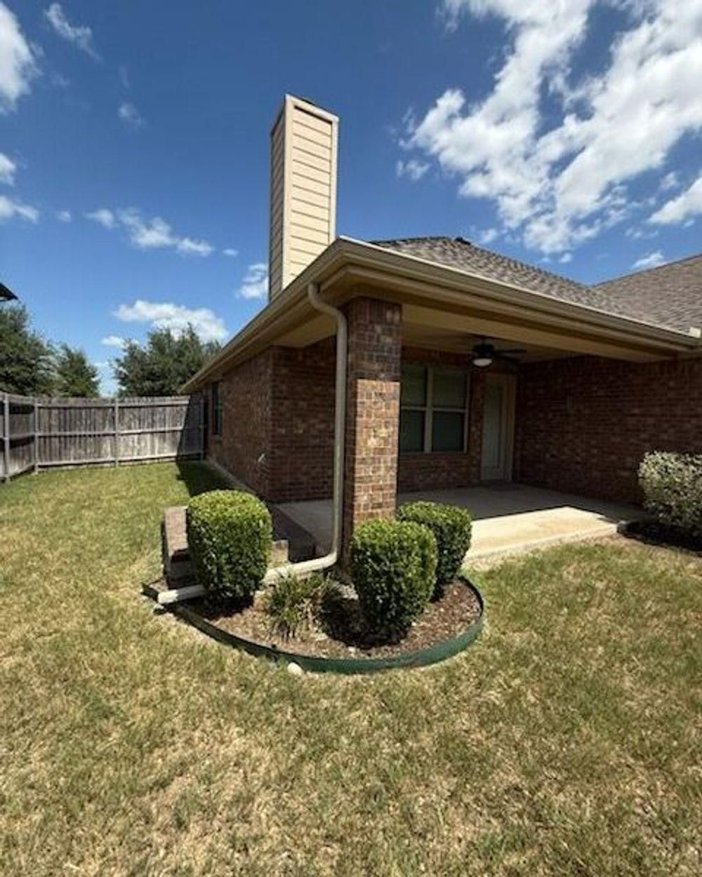 Brick house exterior with patio, chimney, and lawn under a blue sky.