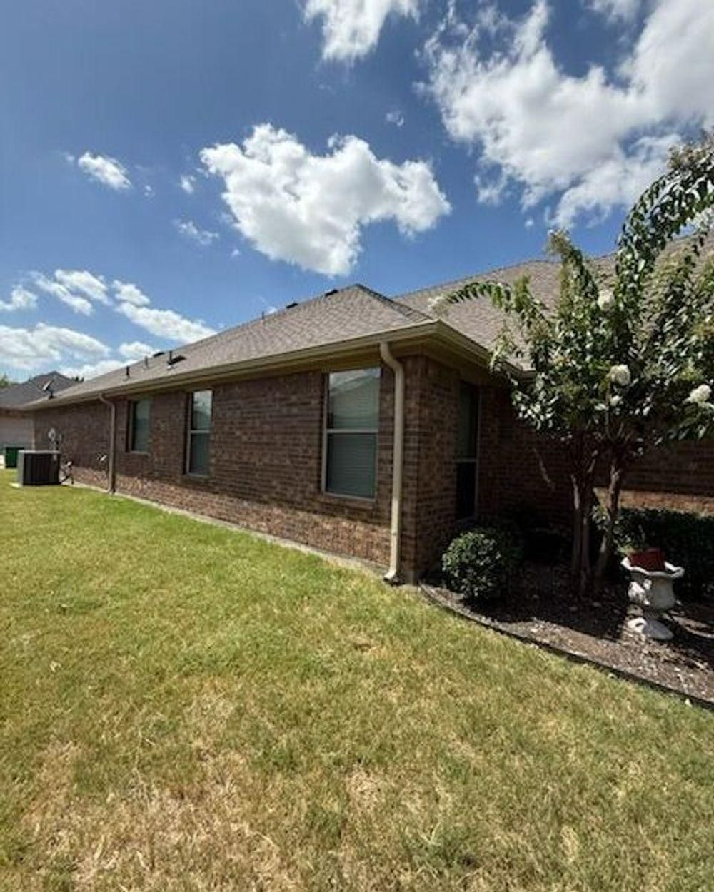 Brick house exterior with a green lawn, windows, and a blue sky with clouds.