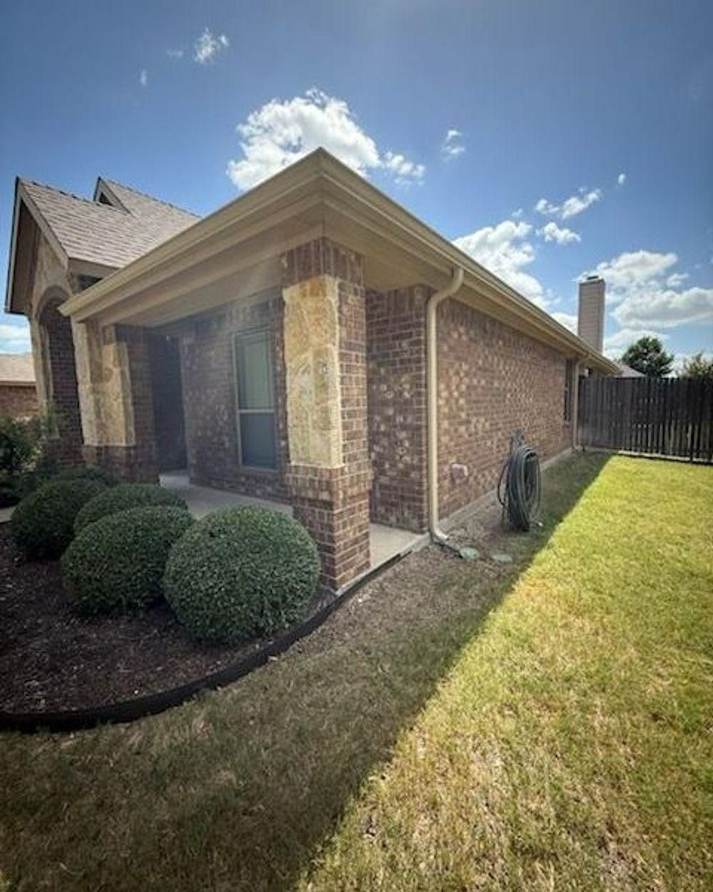 Brick house exterior with brown roof and trim, green lawn, and neatly trimmed bushes.