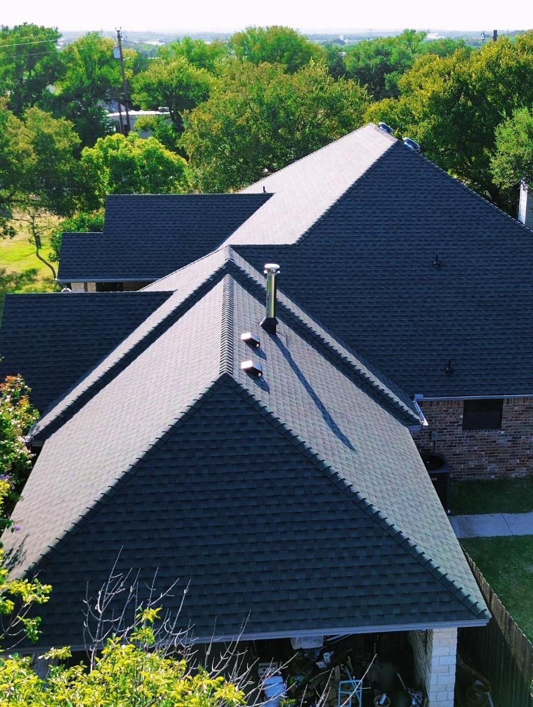 Dark gray asphalt shingle roof on a house, trees in the background.