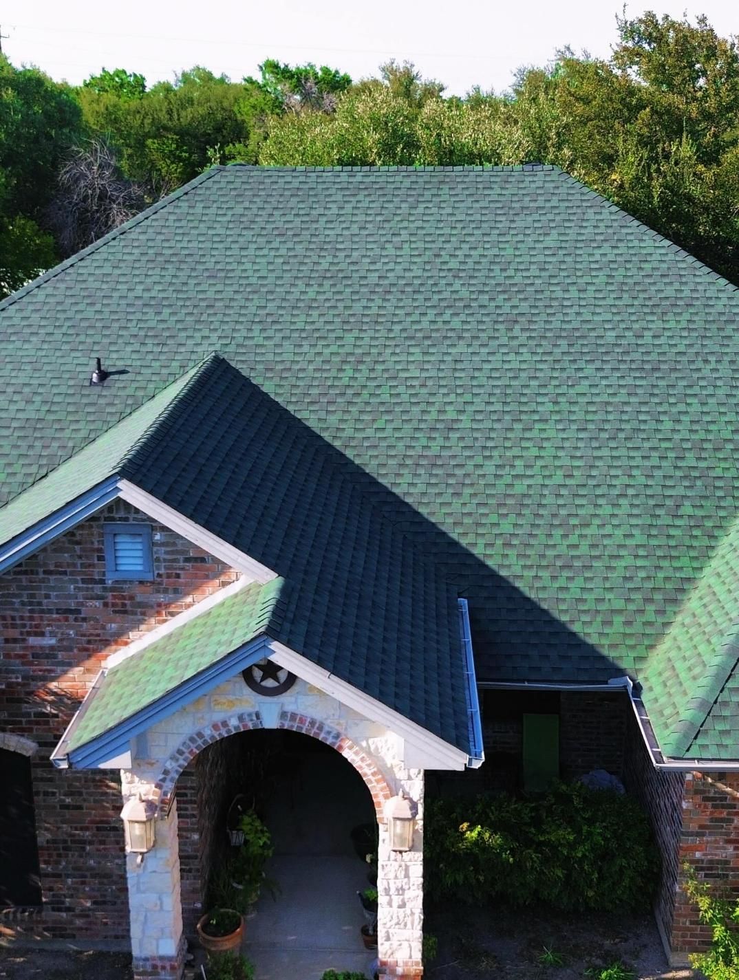 Green shingled roof of a brick house with an arched entrance.