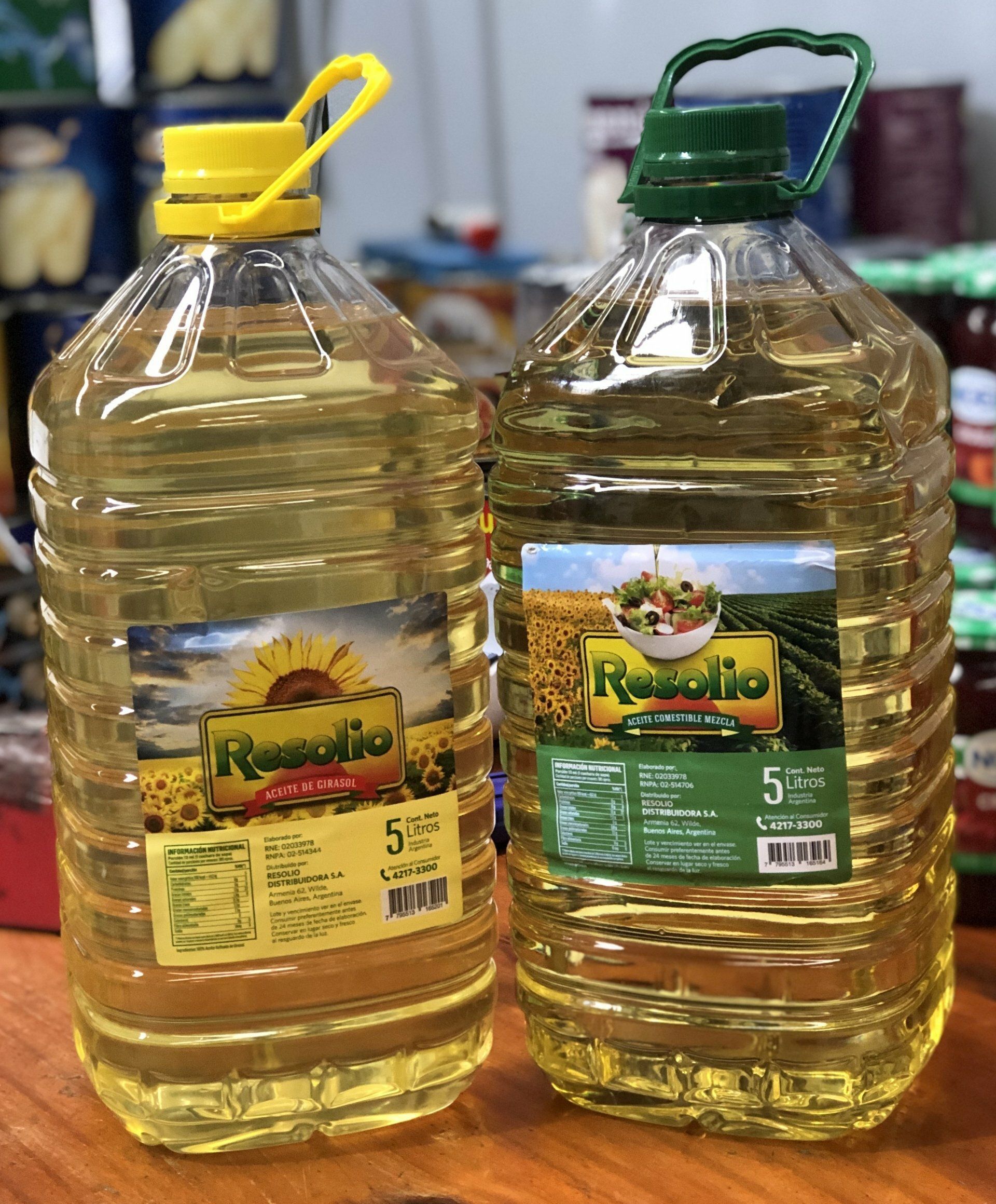 Dos grandes garrafas de plástico de aceite de cocina con tapones amarillos y verdes sobre una mesa.