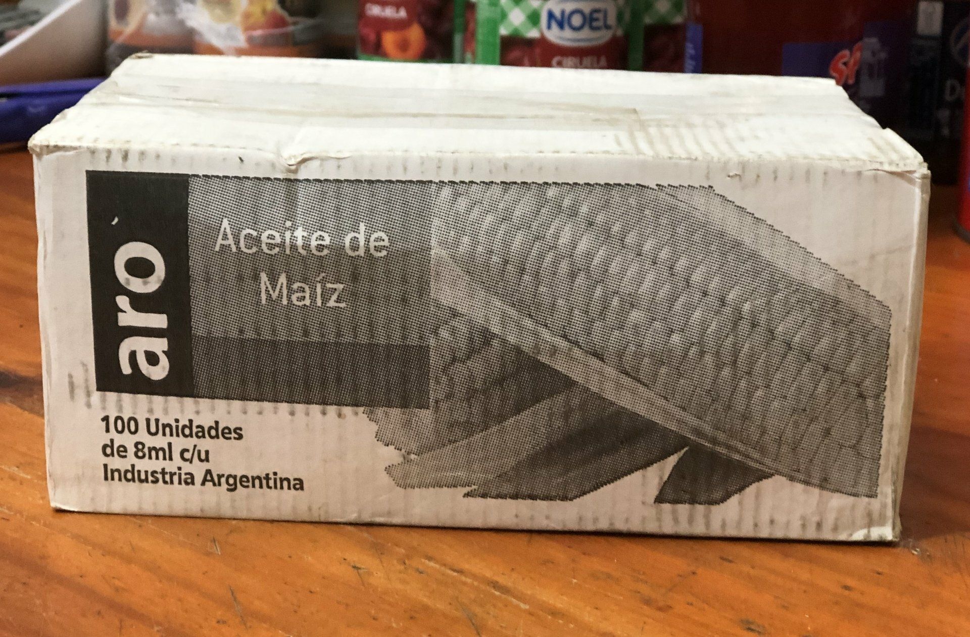 Caja blanca de aceite de maíz sobre una superficie de madera con granos oscuros impresos en la etiqueta.