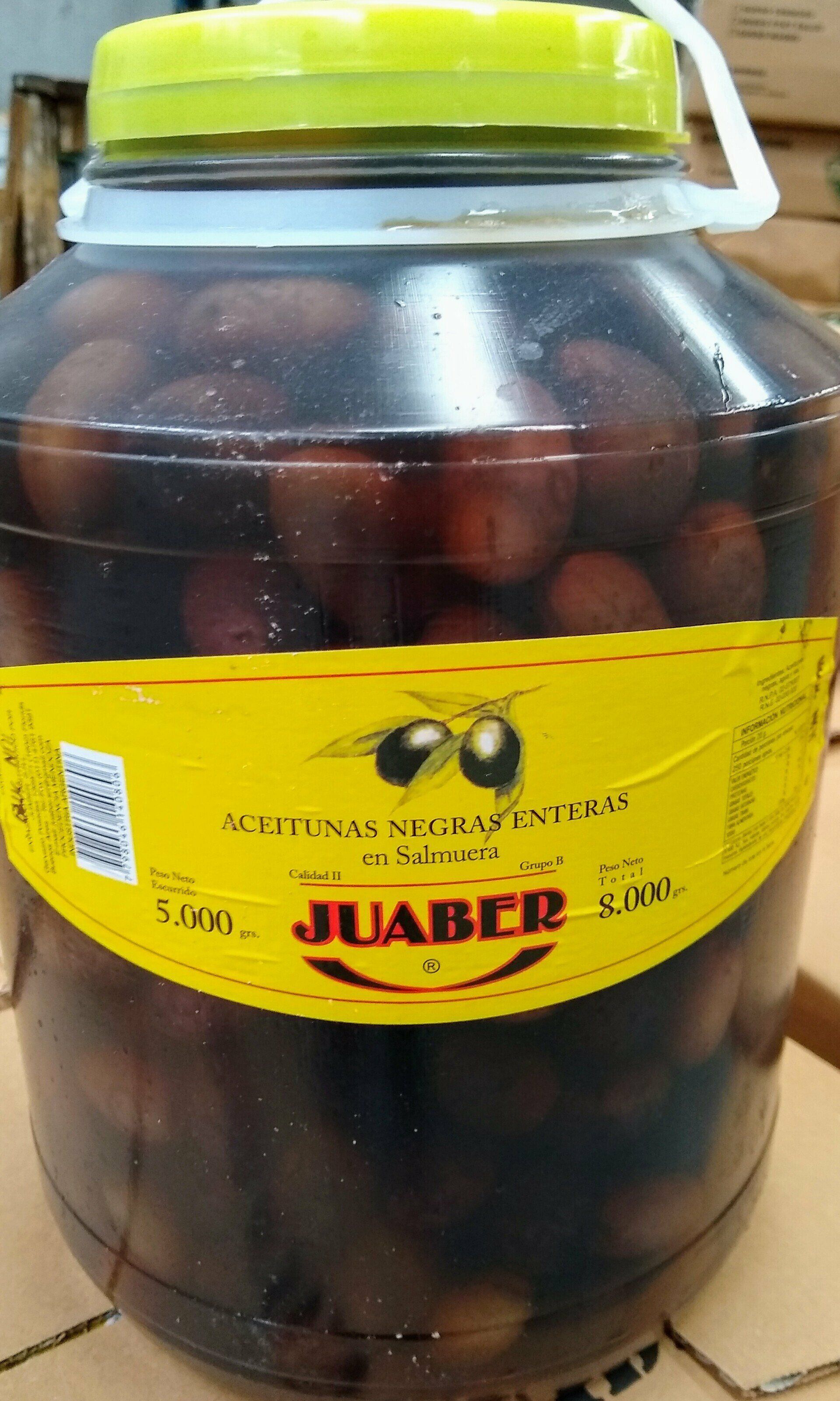 Un tarro grande de fruta en conserva oscura con etiqueta amarilla y tapa verde sobre un mostrador.