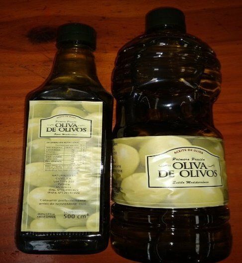 Dos botellas de aceite de oliva sobre una superficie de madera, una cuadrada y otra redonda grande.