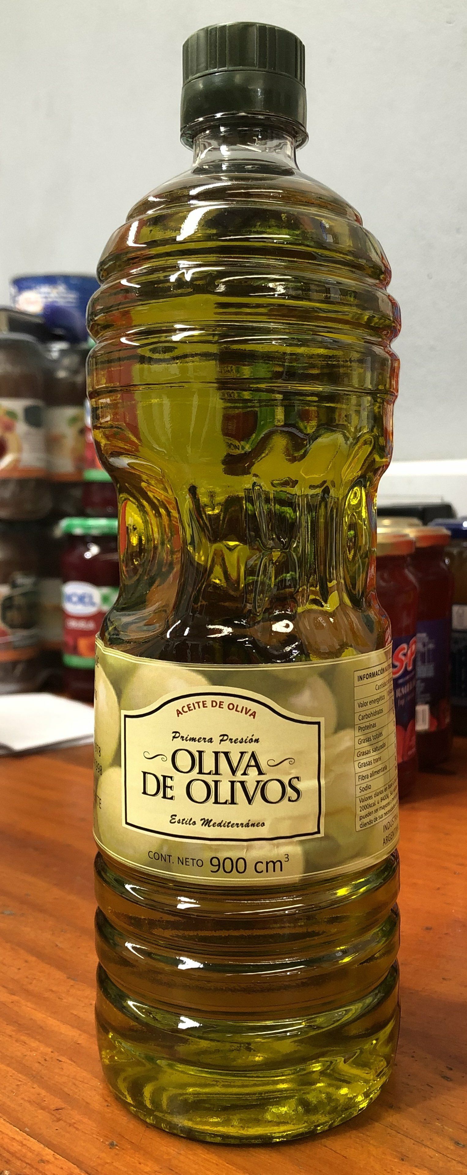 Botella de aceite de oliva con tapón verde sobre una mesa de madera, etiquetada como “Oliya de Olivos”.