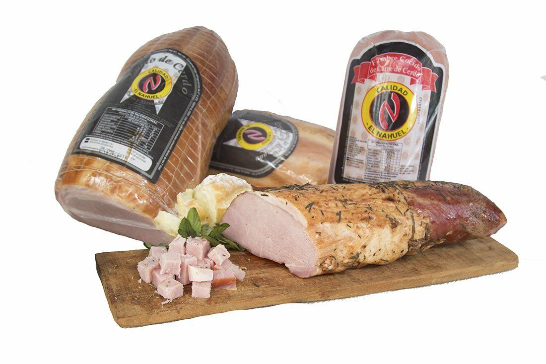 Surtido de embutidos envasados ​​y jamón en lonchas sobre una tabla de madera con guarnición de perejil.